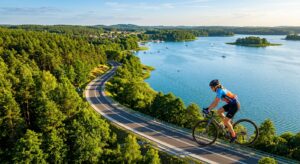 A high-angle, professional editorial shot of a cyclist riding along a scenic, sun-drenched lakeside