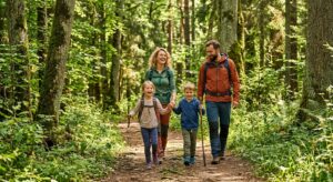 A professional editorial photograph of a joyful family hiking along a scenic trail in the lush, sun-