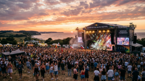 A cinematic, wide-angle shot of a vibrant outdoor summer music festival stage at sunset in the pictu
